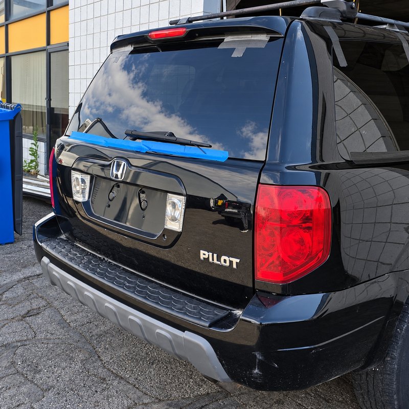 Black Honda Pilot with newly fitted back glass held by blue tape along the bottom