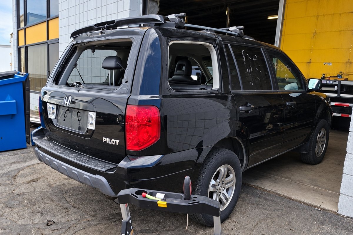 Black Honda Pilot with its back glass and rear side window both missing at a work bay