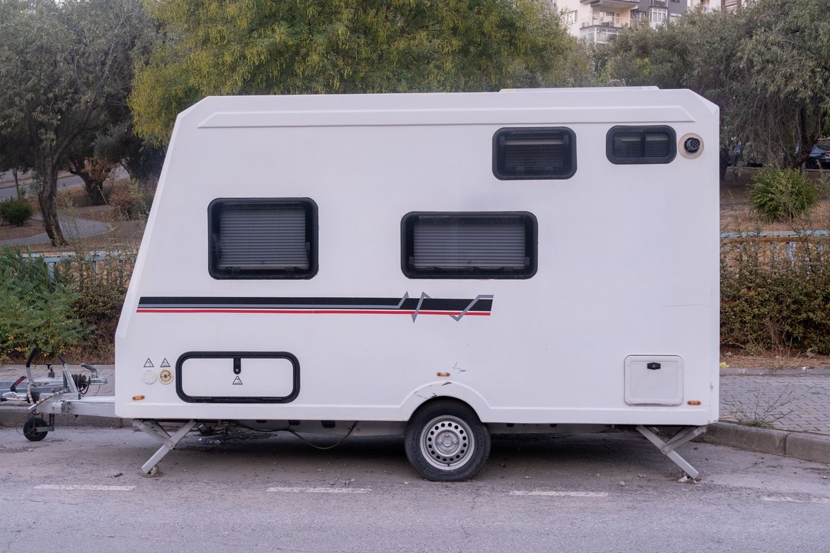 White single-axle travel trailer with four side windows, parked at a curb