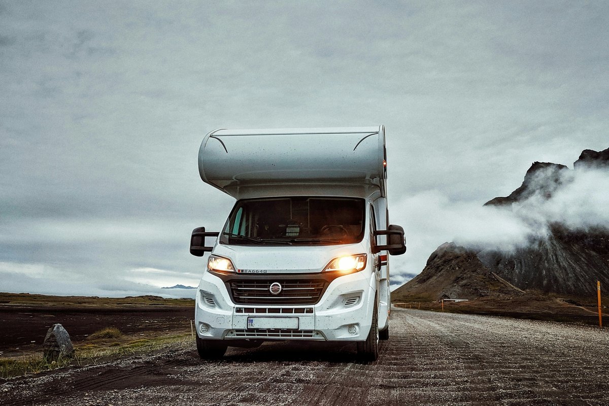 White Class C motorhome on a gravel road, seen from the front with its large one-piece cab windshield