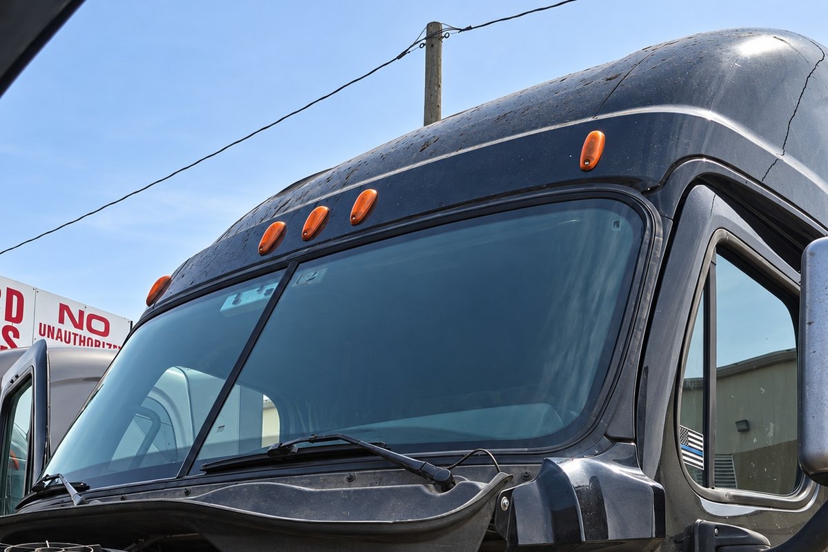 Black Freightliner Cascadia with its hood tilted open below a clean two-piece windshield, one wiper arm raised off the cowl