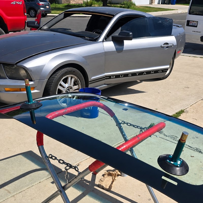 Silver Ford Mustang in a driveway with its windshield removed and the new glass on a stand