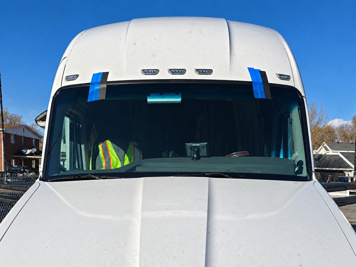 White semi truck cab with a newly fitted one-piece windshield taped at the top