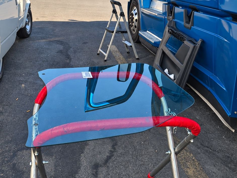 Blue semi truck cab with its door trim panel off and new door glass on a stand