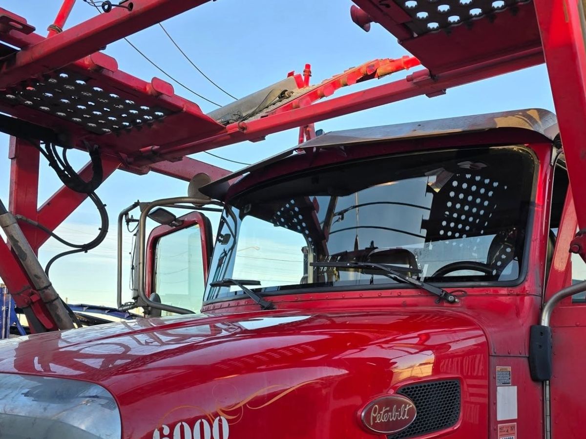 Red Peterbilt car hauler numbered 6000 from the front corner, its windshield clean and in place under the red steel car rack