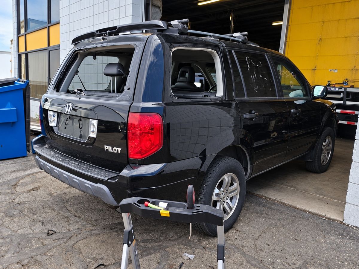 Black Honda Pilot with its back glass and rear side window both missing at a work bay