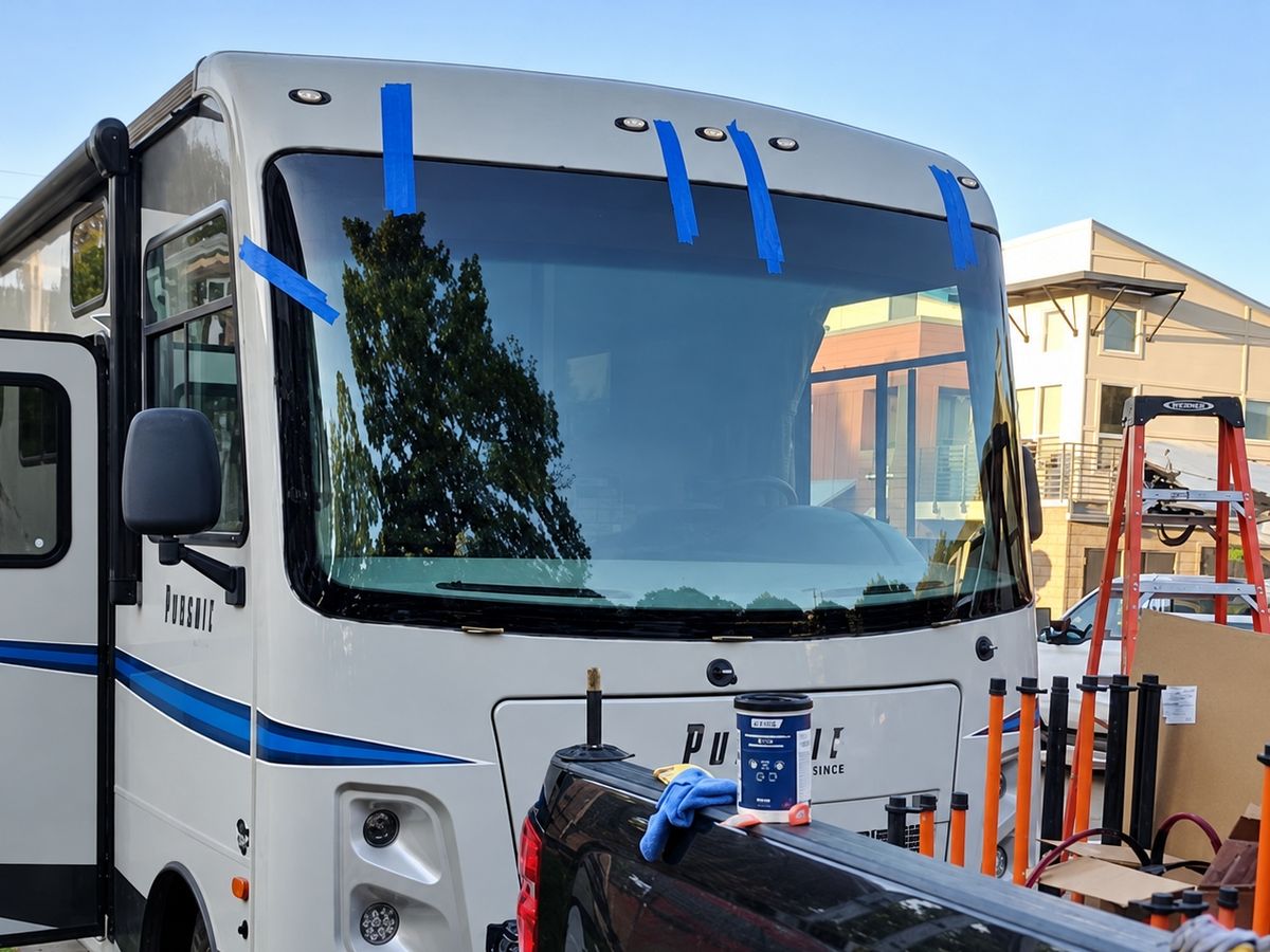 Class A motorhome with a newly fitted one-piece windshield held by blue tape