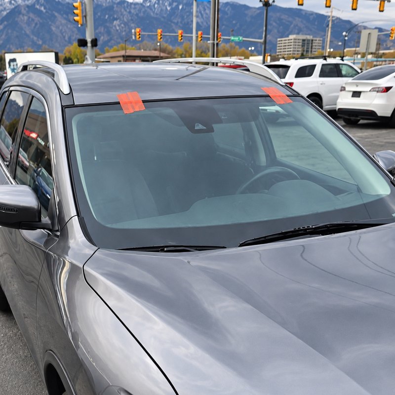 Gray compact SUV with a newly fitted windshield held by orange tape, mountains behind