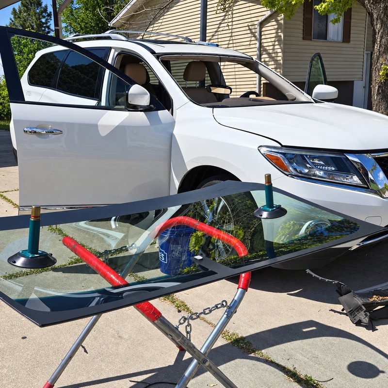 White Nissan SUV with its windshield removed and the new glass on a stand in a driveway
