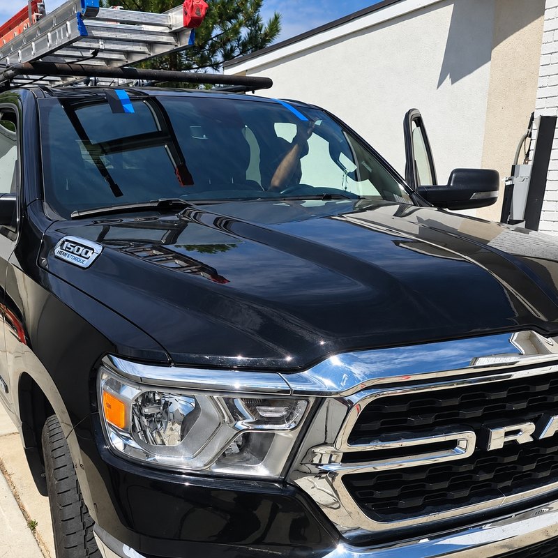 Black Ram 1500 pickup with a ladder rack and a newly fitted windshield held by blue tape