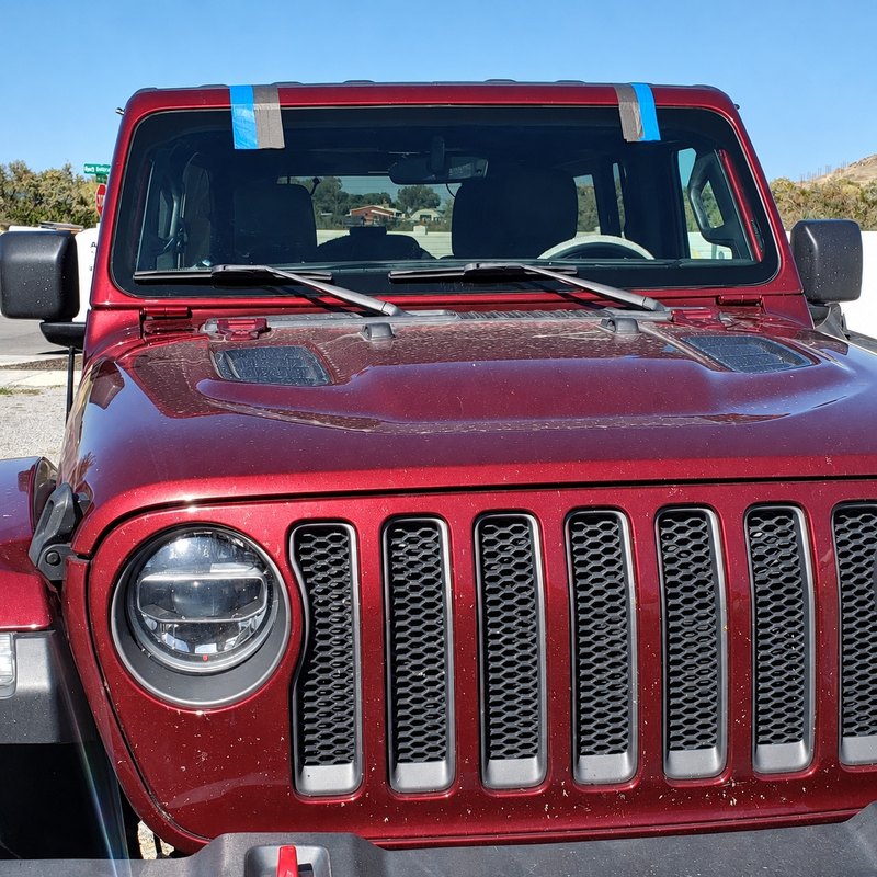 Dark red Jeep Wrangler with a newly fitted windshield and a dusty, speckled hood